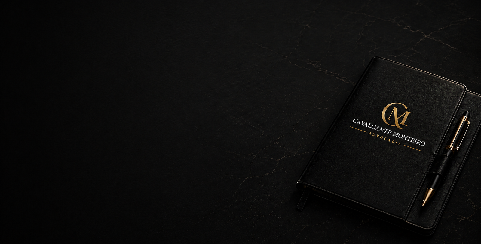 Caderno preto com monograma dourado e caneta sobre superfície escura